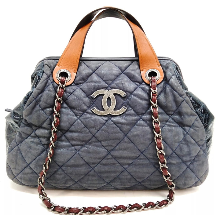 A close-up photo of a Chanel In The Mix tote bag in a vibrant blue color. The bag is made of quilted leather and features a chain-link strap and a gold Chanel logo on the front