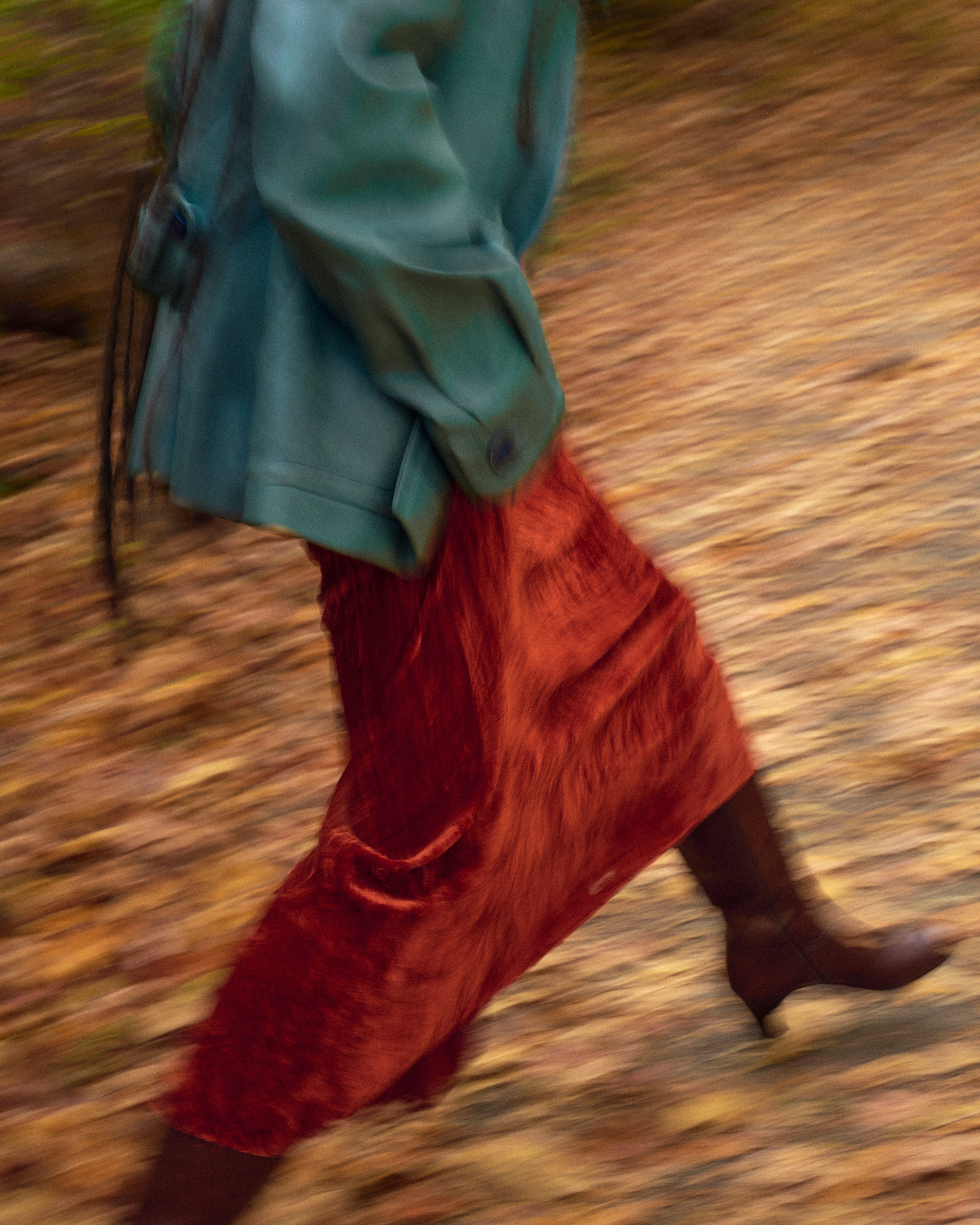 Person wearing a green vintage chloe jacket and 1930's burnt orange velvet dress with feerragamo boots  - editorial shot on a blurred natural background