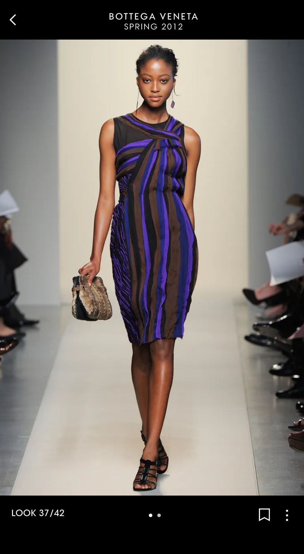 Model wearing a striped dress on a runway with Bottega Veneta branding.