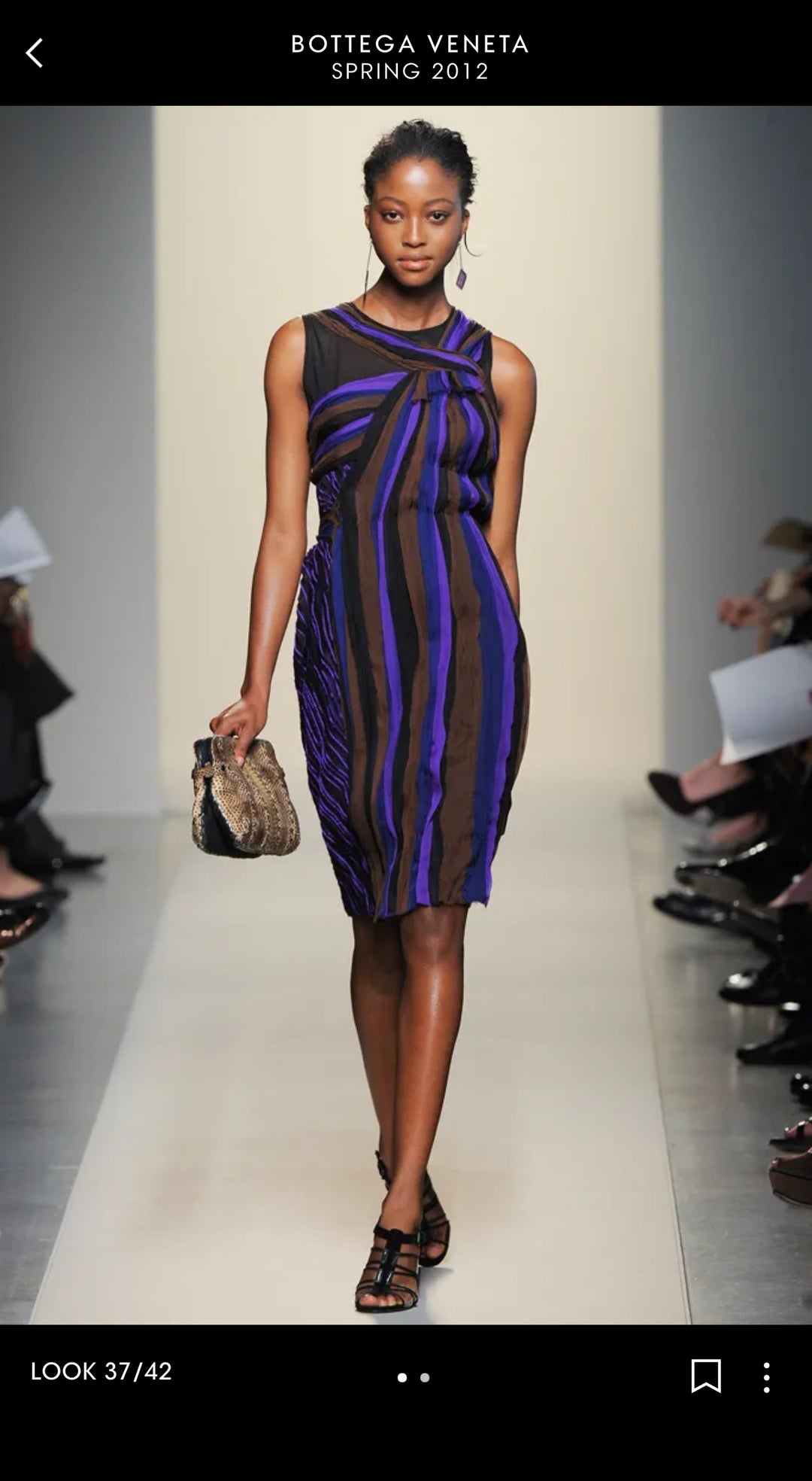 Model wearing a striped dress on a runway with Bottega Veneta branding.