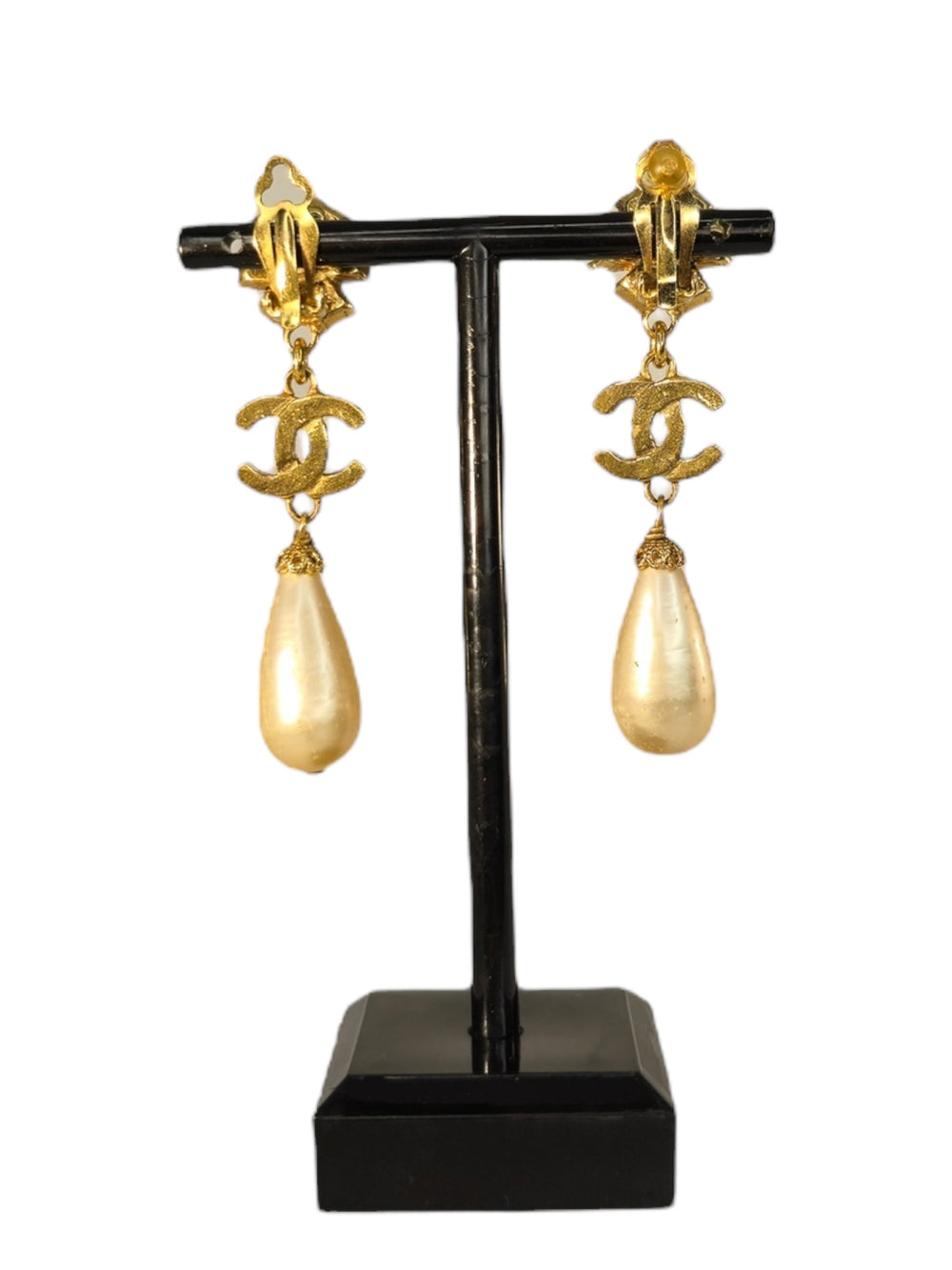 Gold earrings with pearl drops on a black stand against a white background
