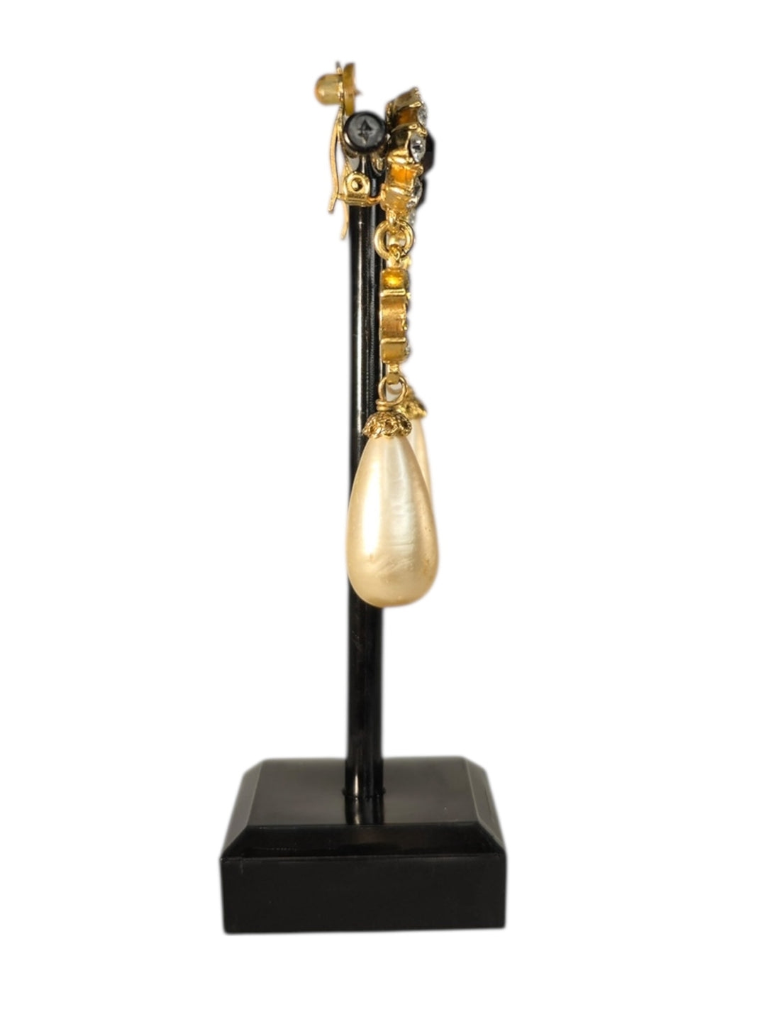 Gold Chanel teardrop earring on a black stand against a white background