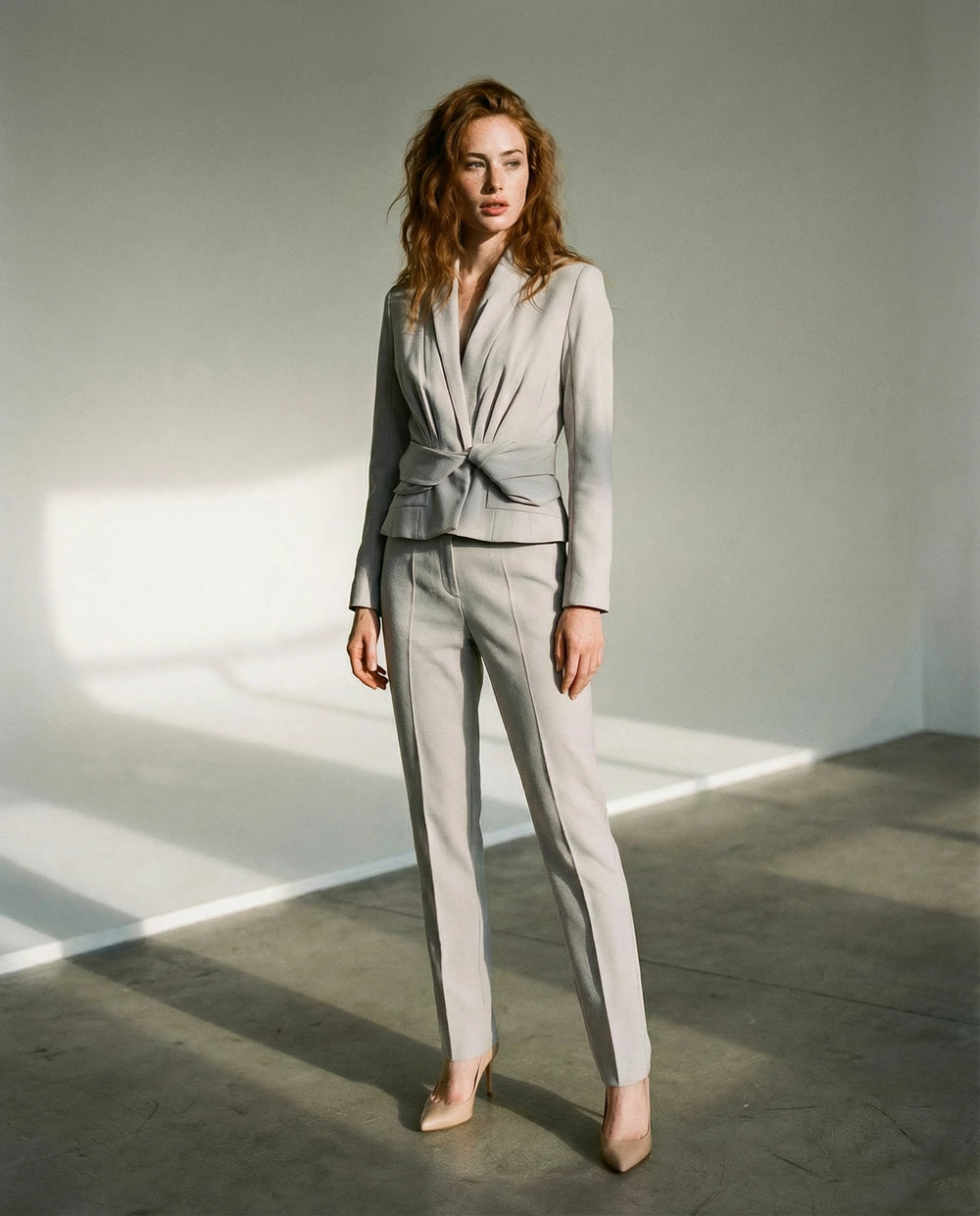 Woman wearing a Christian Dior by John Galliano twisted grey pants suit standing in a minimalistic setting with soft lighting.