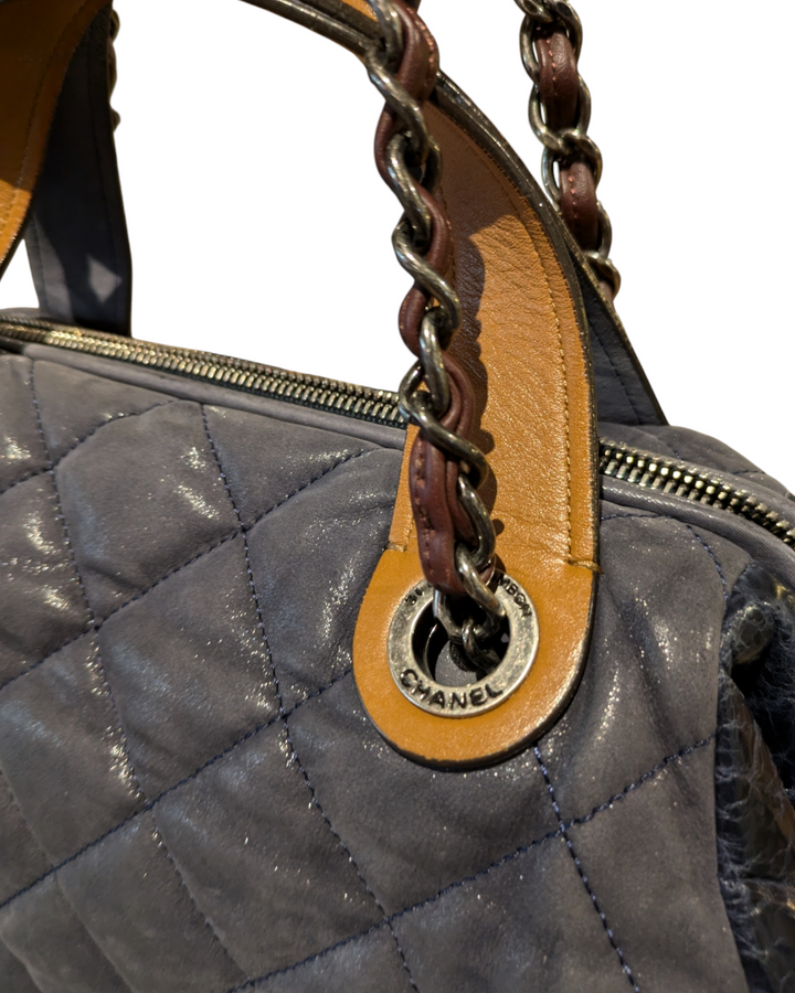 A close-up photo of a Chanel In The Mix tote bag in a vibrant blue color. The bag is made of quilted leather and features a chain-link strap and a gold Chanel logo on the front