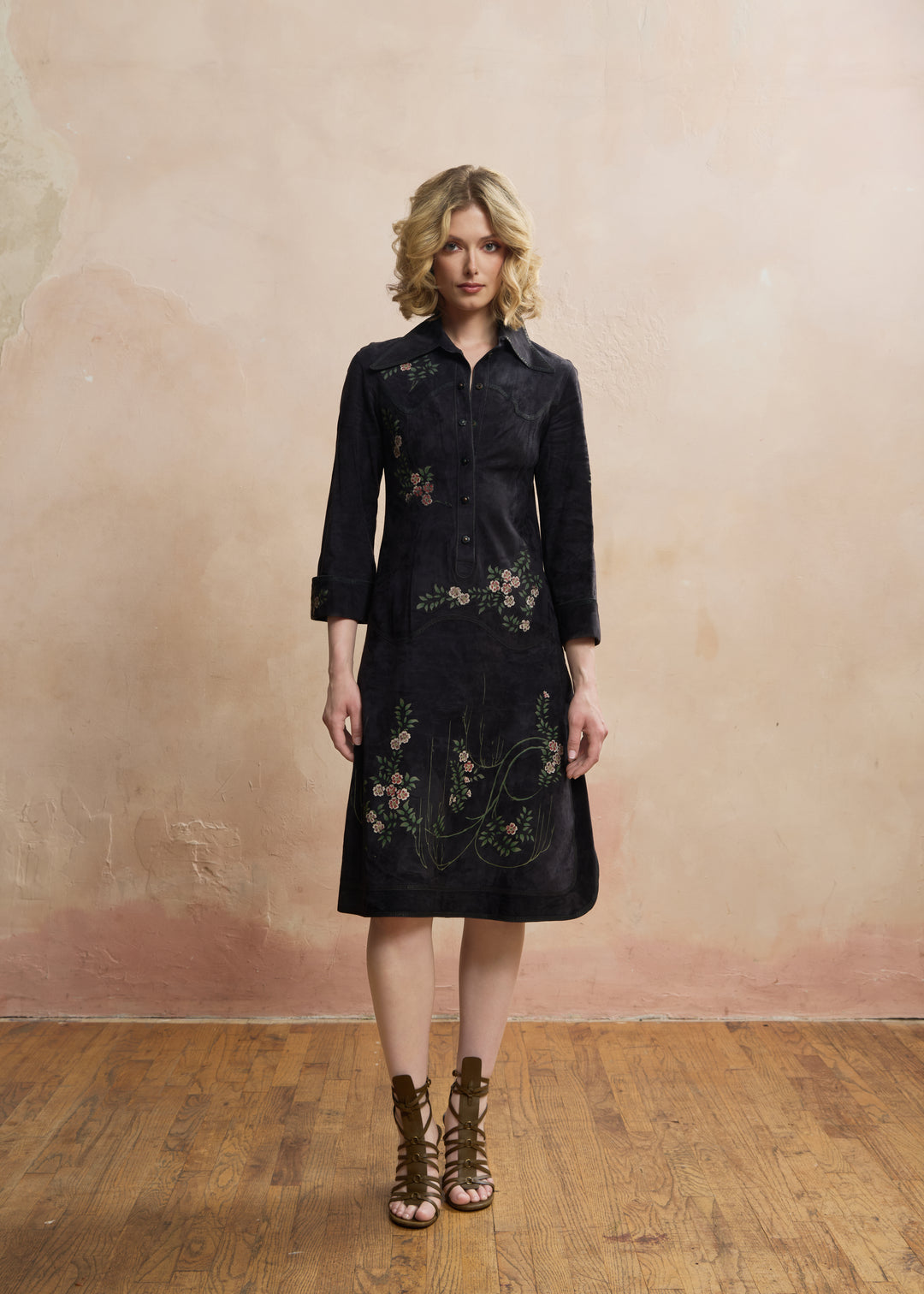 A woman stands in a studio wearing a dark midi shirt dress with floral embroidery and brown lace-up ankle boots against a textured beige wall and wooden floor. ROBERTO CAVALLI RERACKED VOGUE 1970'S PAINTED SUEDE COLLECTION RARE - FASHION HISTORY MET MUSEUM