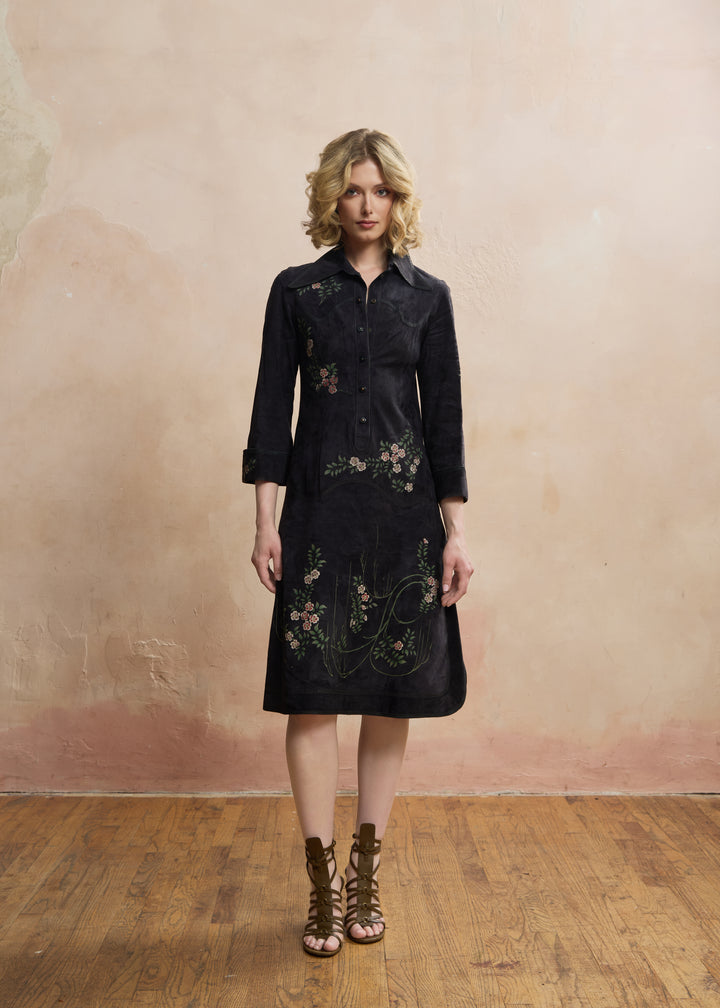 A woman stands in a studio wearing a dark midi shirt dress with floral embroidery and brown lace-up ankle boots against a textured beige wall and wooden floor. ROBERTO CAVALLI RERACKED VOGUE 1970'S PAINTED SUEDE COLLECTION RARE - FASHION HISTORY MET MUSEUM