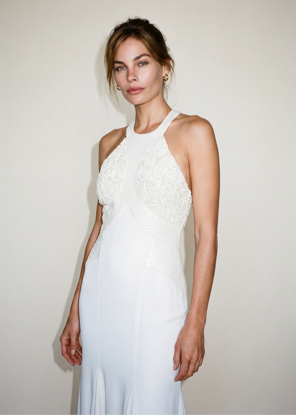 Woman wearing a white halter-neck dress against a plain background
