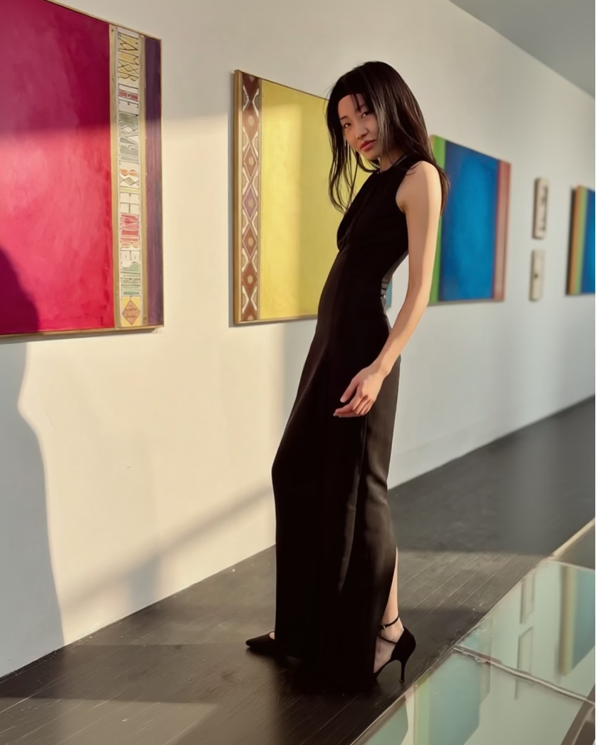 Woman in a black dress standing in an art gallery with colorful paintings on the wall.