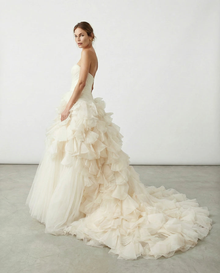Woman wearing a white vintage Vera wang wedding dress with a ruffled skirt on a plain background