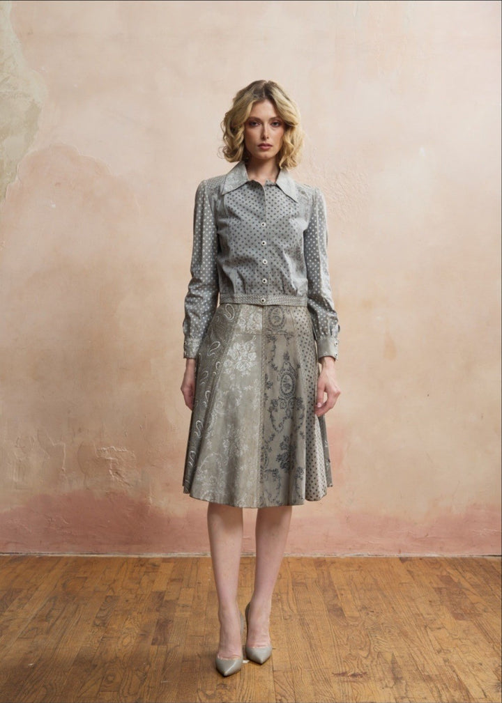A woman models a matching two-piece dress set featuring a long-sleeve collared shirt and a flared A-line skirt, both in a gray and beige paisley jacquard pattern, set against a textured beige plaster wall and wooden floor.