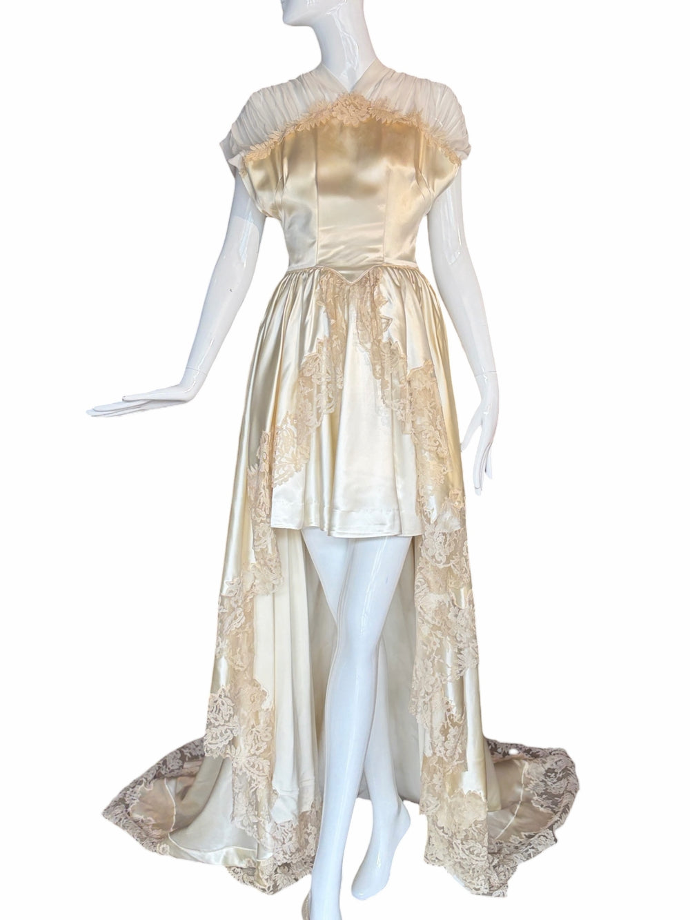 RERACKED vintage cream satin high-low bridal gown with delicate lace trim and sheer pleated cap sleeves on a mannequin.
