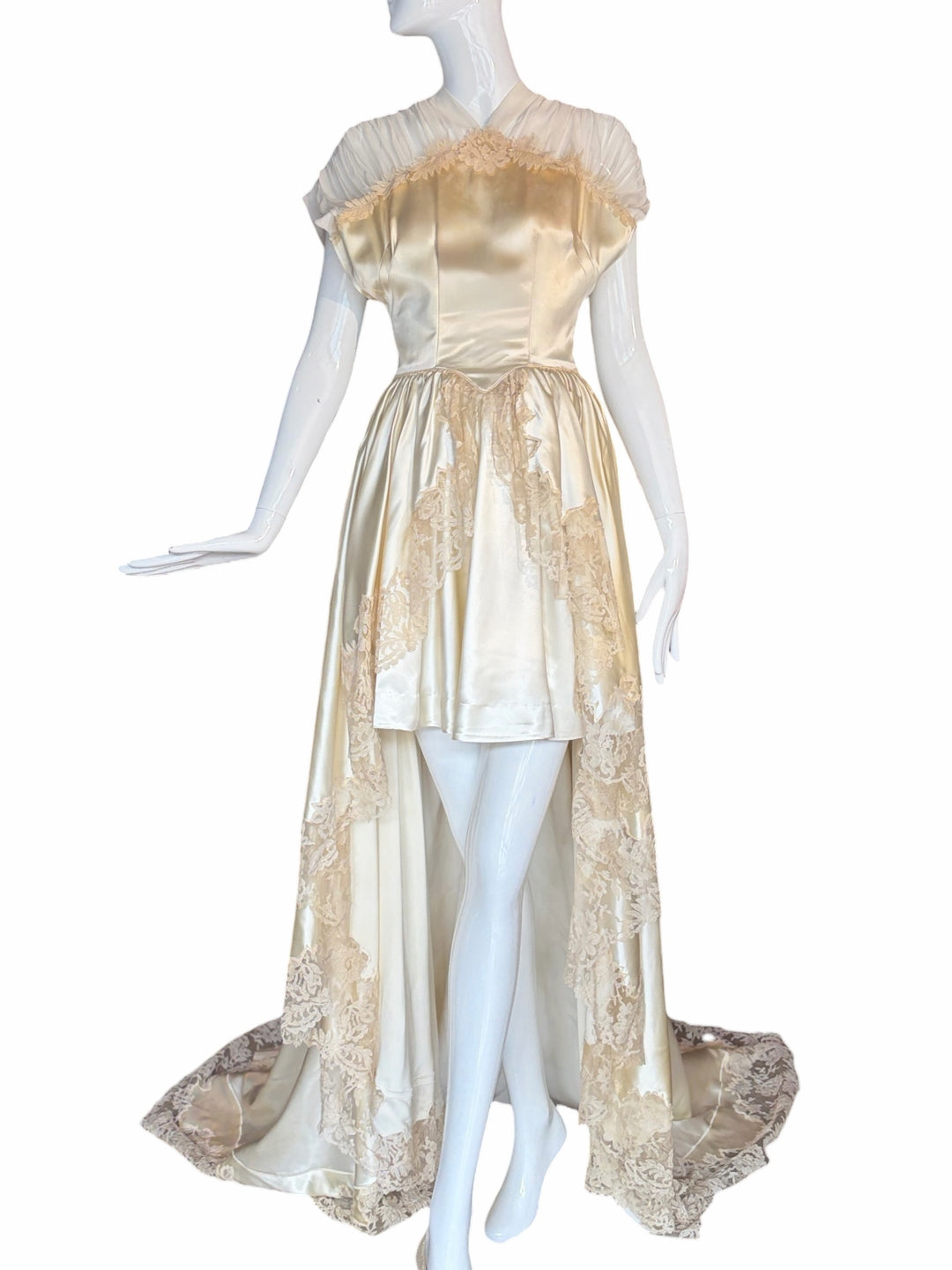 RERACKED vintage cream satin high-low bridal gown with delicate lace trim and sheer pleated cap sleeves on a mannequin.