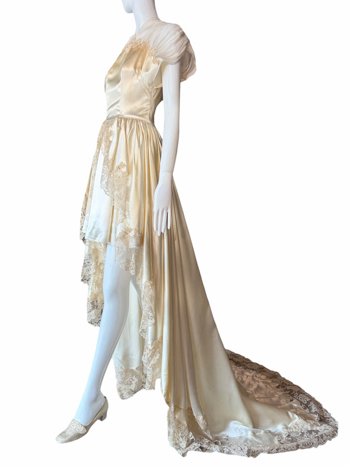 RERACKED vintage cream satin high-low bridal gown with delicate lace trim, pleated cap sleeves, and a long train.
