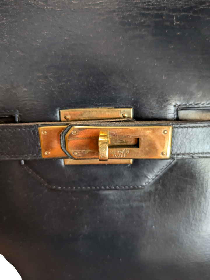 Black leather Hermes handbag with trapezoidal shape and signature turn-lock closure, hold hardware, lock and key attached