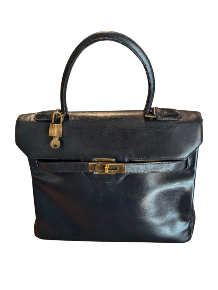 Black leather Hermes handbag with trapezoidal shape and signature turn-lock closure, hold hardware, lock and key attached